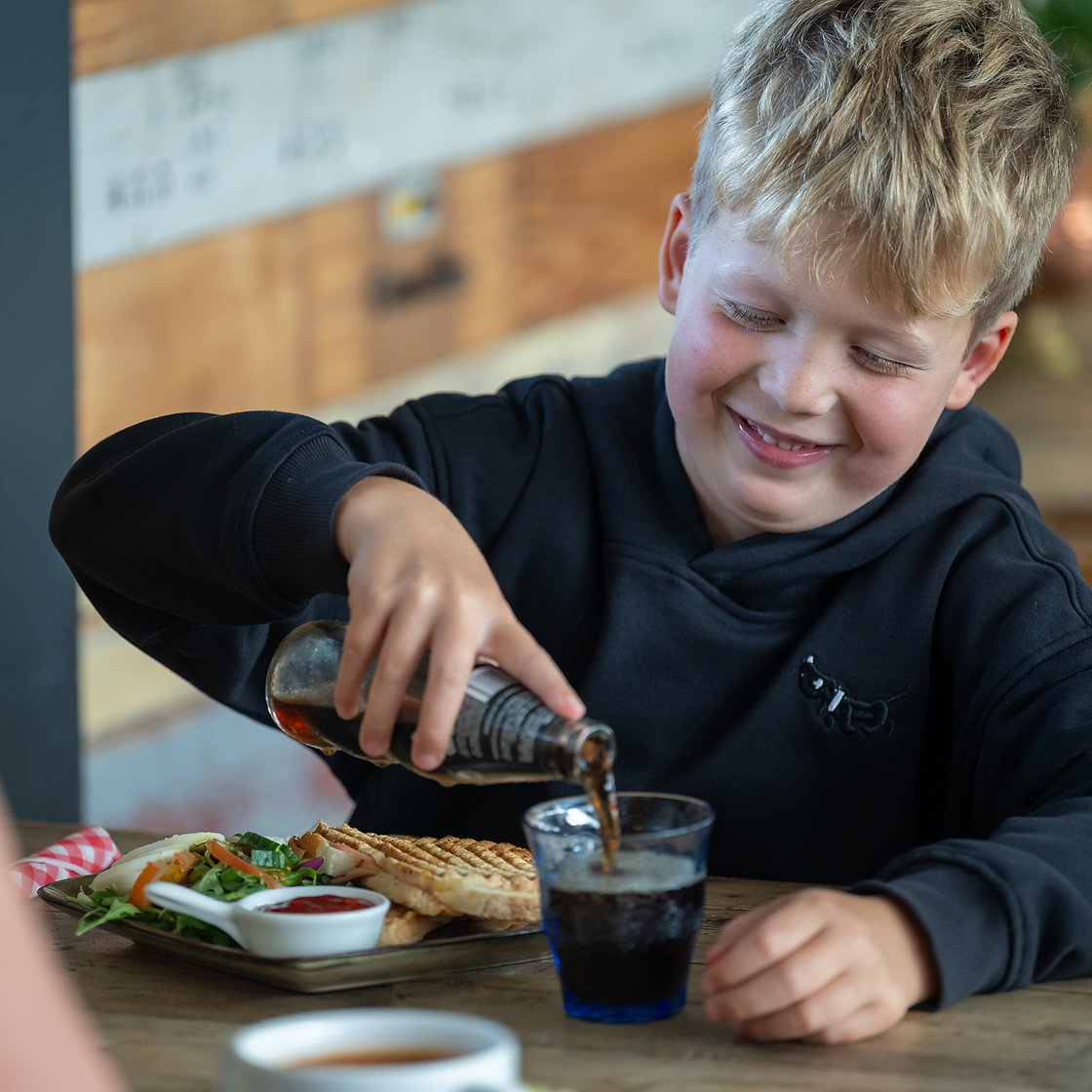 een jongen schenkt een glas fris in bij zijn tosti in Eetcafé Wiegman
