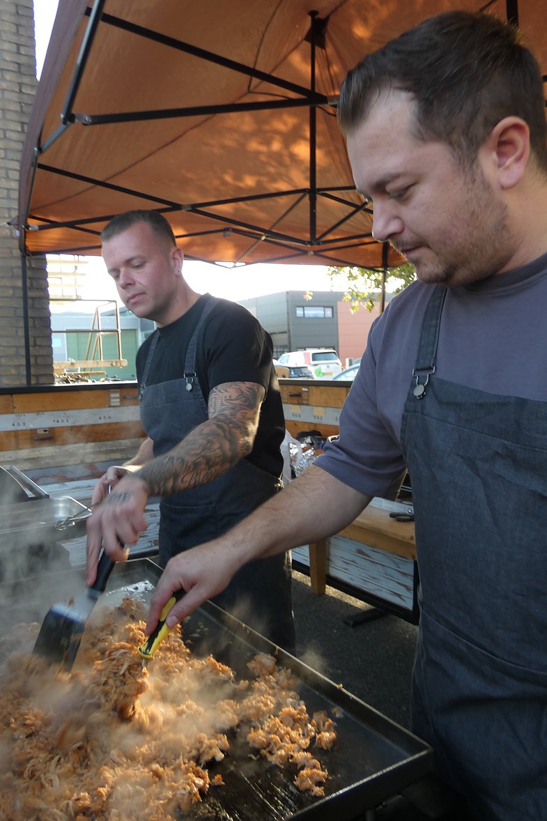 twee koks bakken vlees op de bakplaat onder de partytent tijdens een barbecue