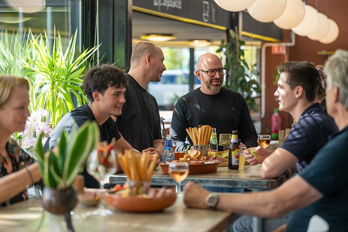 een groot gezelschap aan tafel met borrelplanken en drankjes