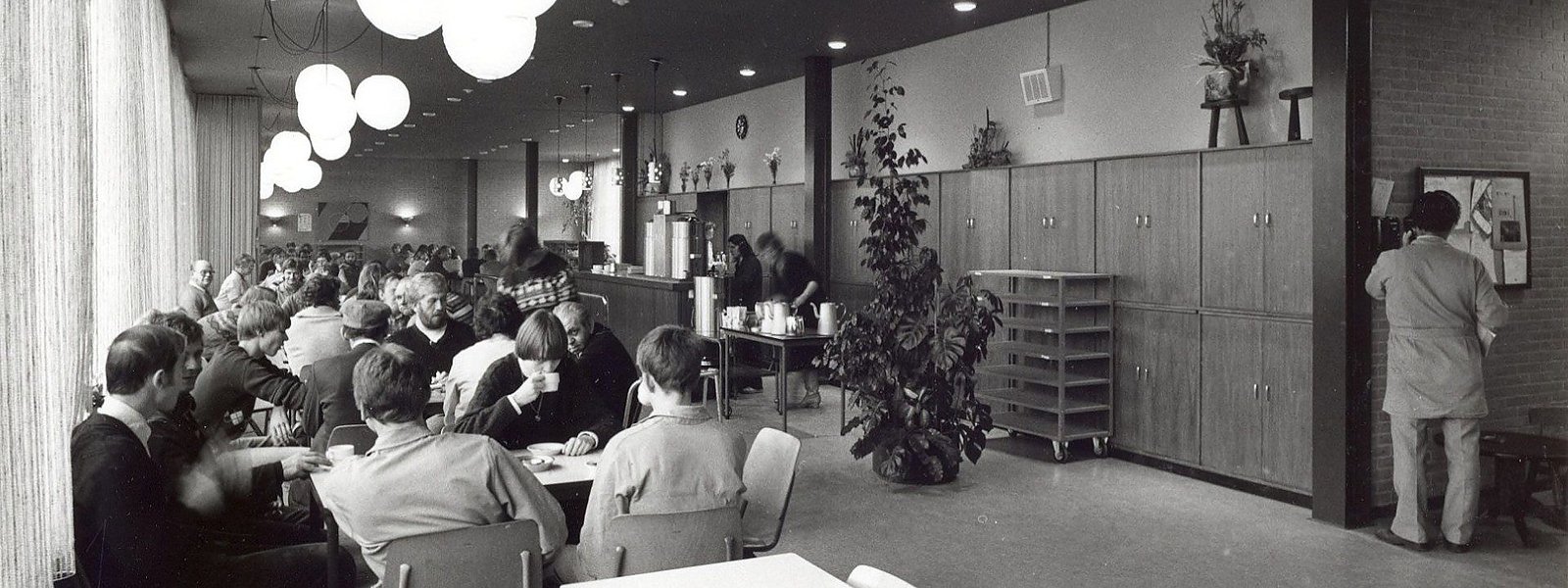 de kantine van dit pand in de jaren zestig, met lange tafels vol mensen tijdens de pauze
